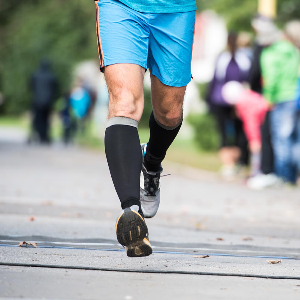 Man running in shorts and compression socks, showcasing support for leg health and comfort during physical activity.